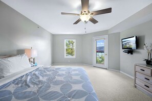 Une chambre à coucher avec un lit, un ventilateur de plafond, une télévision, une commode et une fenêtre.
