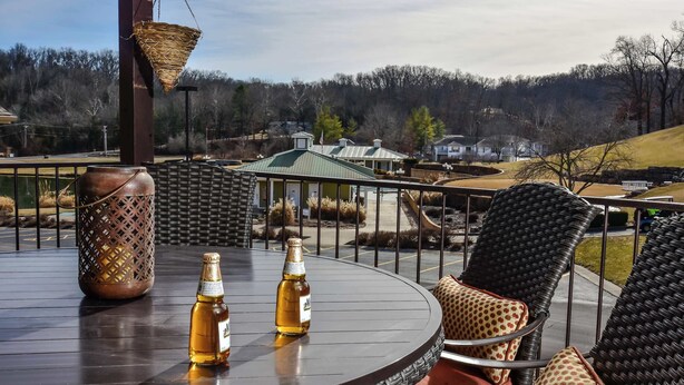 A round table with two bottles of beer, a woven basket, and wicker chairs with patterned cushions. - Birdie's Bliss 2BR Condo Sleeps 6! (Lake Ozark)