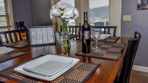 A dining table set with placemats, plates, a bottle of wine, and a vase of flowers. - Birdie's Bliss 2BR Condo Sleeps 6! (Lake Ozark)