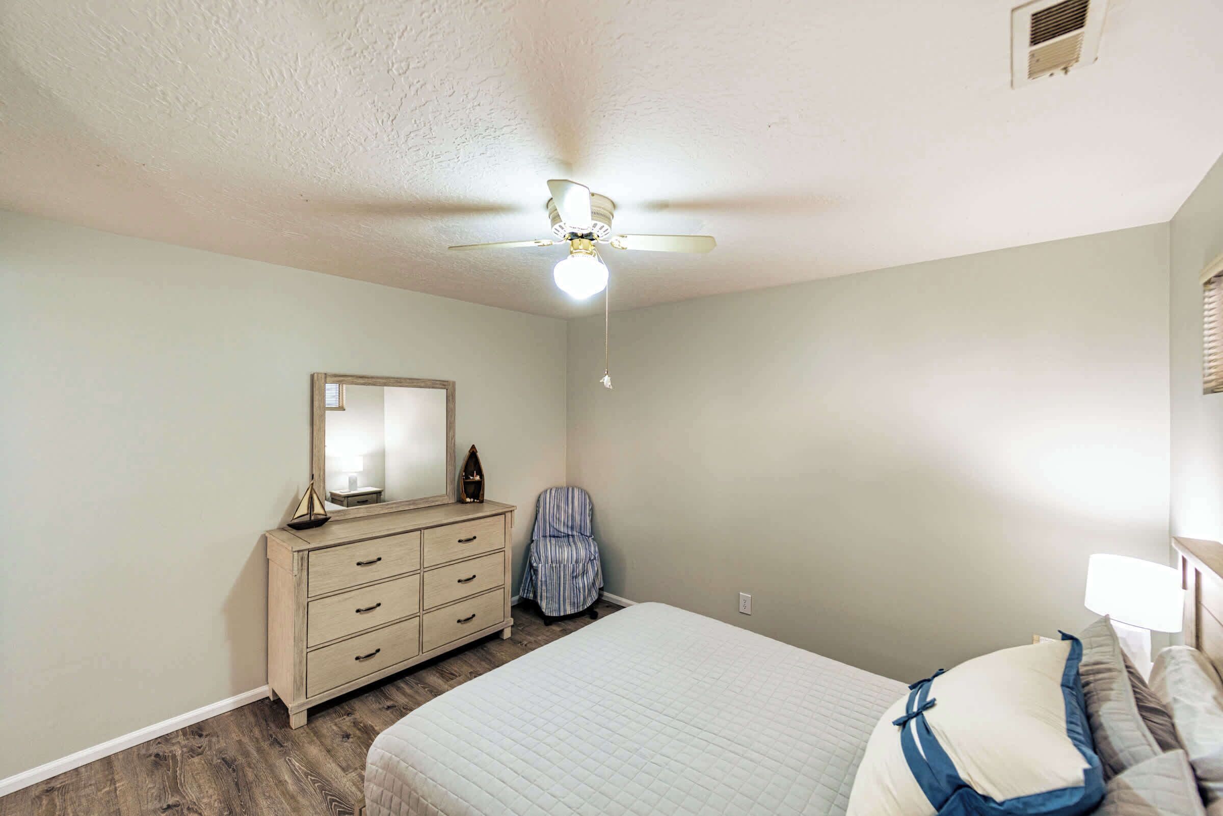 A bedroom with a bed, a dresser, a chair, and a ceiling fan.