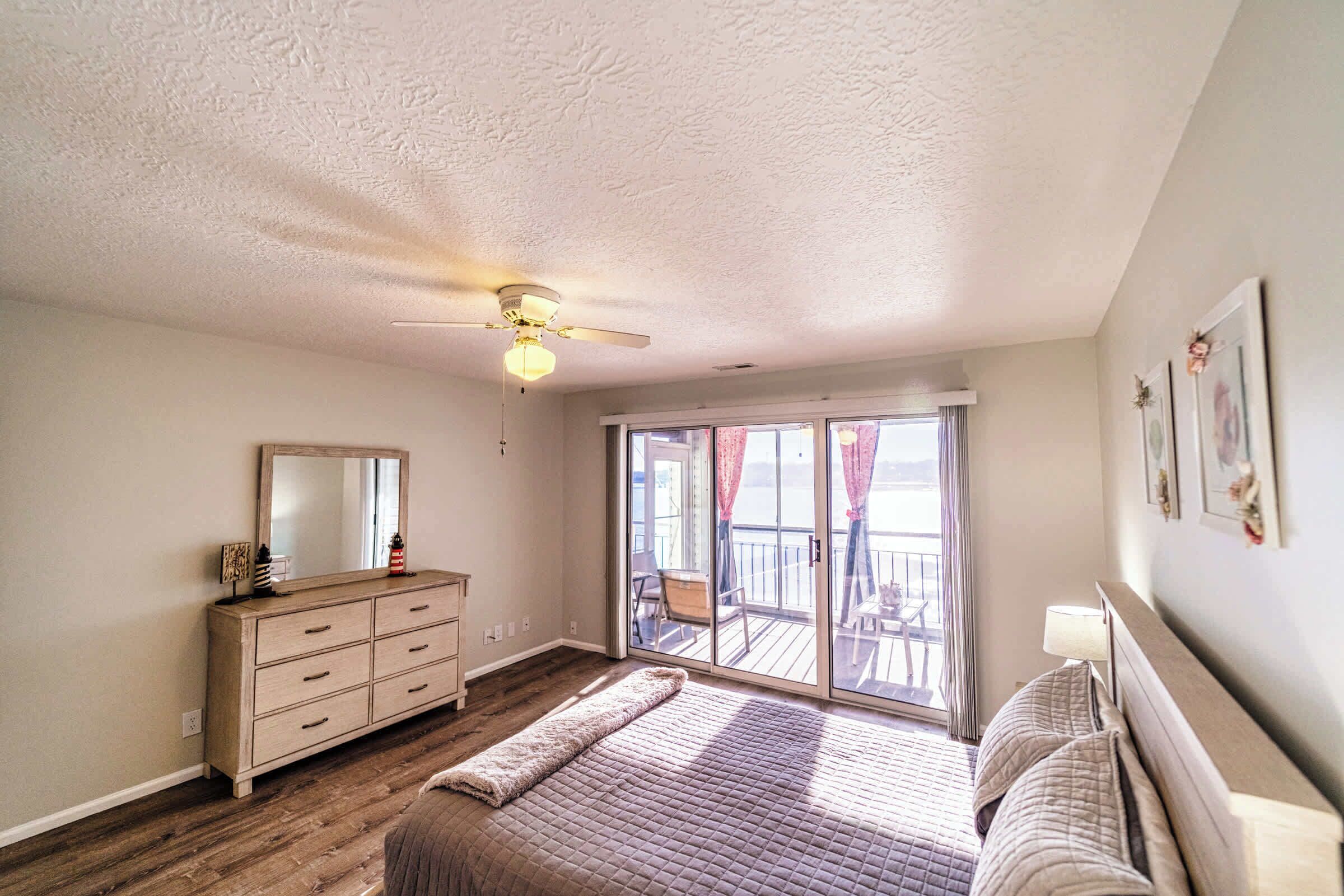 A bedroom with a large bed, a dresser, a ceiling fan, and a sliding glass door leading to a balcony.