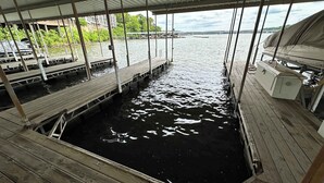 Eine überdachte Anlegestelle mit Holzstegen über dem Wasser, ein Boot an der rechten Seite vertäut und ein Blick auf eine Brücke sowie Gebäude in der Ferne.