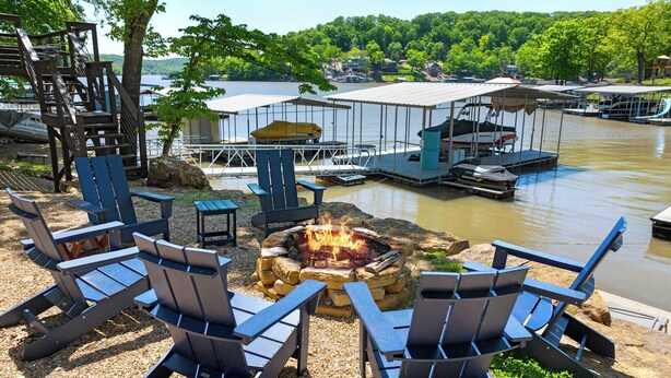 A lakeside deck with Adirondack chairs, a fire pit, and docked boats.