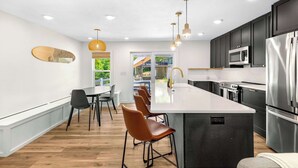 A modern kitchen with a central island, dark cabinets, stainless steel appliances, and a dining area with chairs and a table.