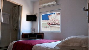 A bedroom with a bed, a TV mounted on the wall, and a window with a view of buildings. - HOTEL Des ARTS AIX Hyper Centre (Aix-en-Provence)