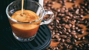 A clear glass cup of coffee with a handle, placed on a black coaster. - HOTEL Des ARTS AIX Hyper Centre (Aix-en-Provence)