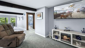 Ett modernt vardagsrum med en stor platt-TV, en bekväm soffa, en öppen spis och en balkong med utsikt.