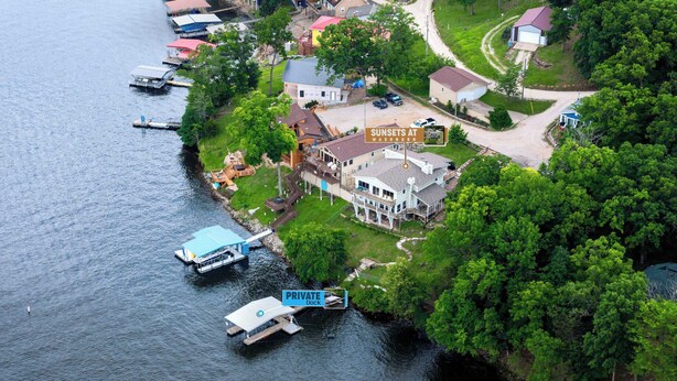En vy från ovan över en fastighet vid sjön, med en privat brygga, ett stort hus med en veranda och en skylt som visar texten ”Solnedgångar vid Washburn”.