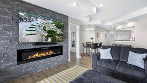 Ein modernes Wohnzimmer mit Kamin, einem großen Fernseher an einer Ziegelwand und einem grauen Sofa mit gemusterten Kissen.