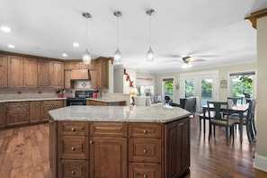 A spacious kitchen with wooden cabinets, granite countertops, pendant lighting, and a dining area with a table and chairs.