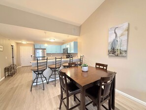 A dining area with a wooden table and chairs, a kitchen in the background, and a painting on the wall. - Highland Lake View – Incredible Location! (Lake Ozark)