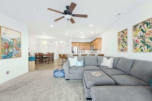 A modern living room with a grey sectional sofa, a ceiling fan, and a dining area with wooden chairs. - Panoramic Sunset Escape – Waterfront Condo for 7! (Osage Beach)