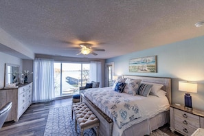 A bedroom with a bed, bedside table, nightstand, bench, and a view through a large window.