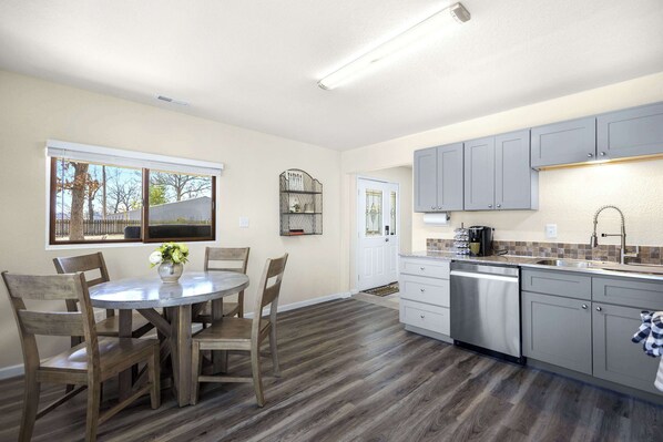 A kitchen with wooden flooring, a dining table with chairs, and grey cabinets.