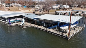 Un bote amarrado con una zona cubierta y un tobogán pequeño, rodeado de agua y estructuras de muelle.