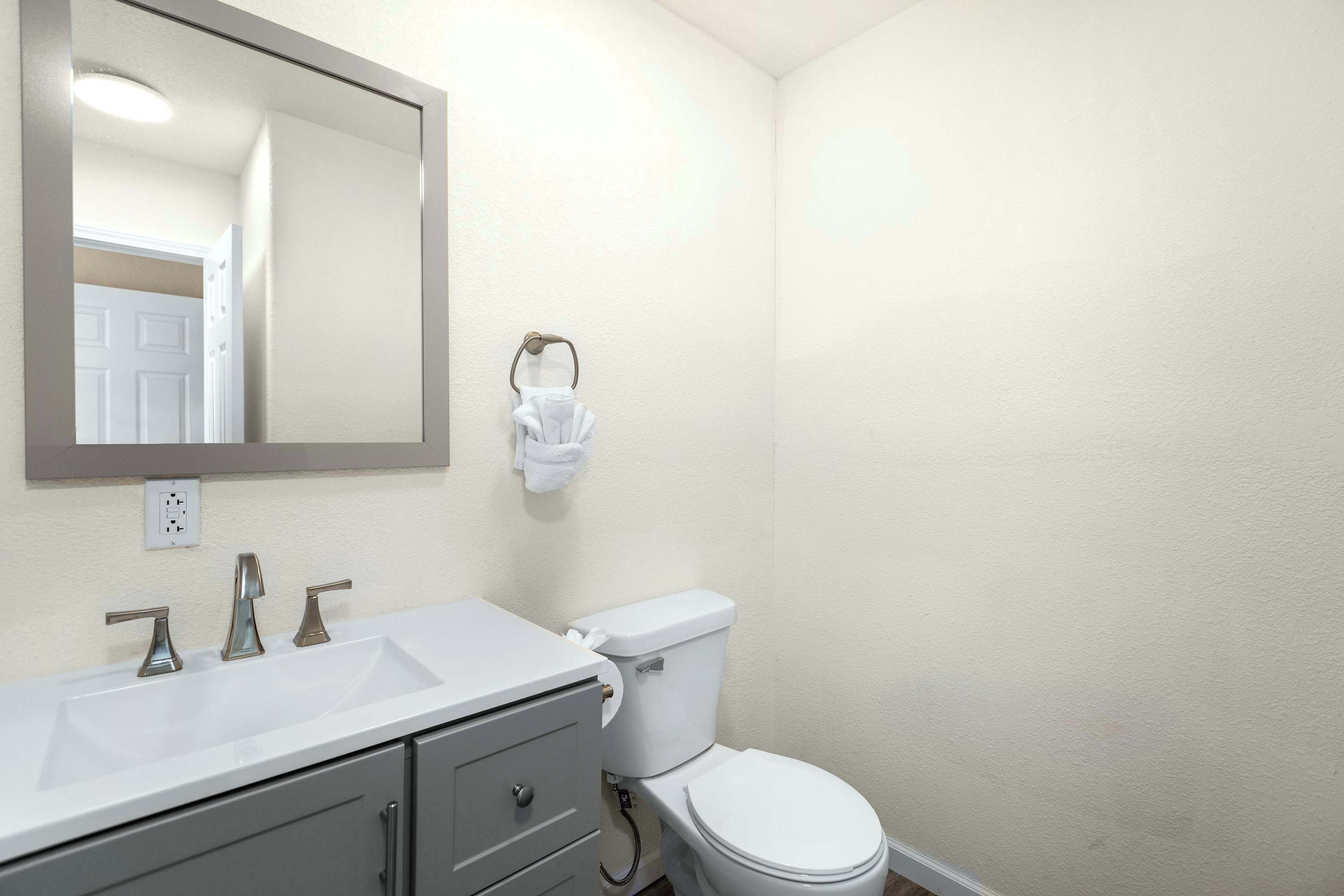 A bathroom with a white sink, three faucets, a toilet, and a mirror.