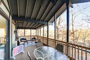 A covered outdoor seating area with a glass table and chairs, a wooden fence, and a view of trees. - Serenity Now – Quiet 4 BDR Next to Margaritaville! (Osage Beach)