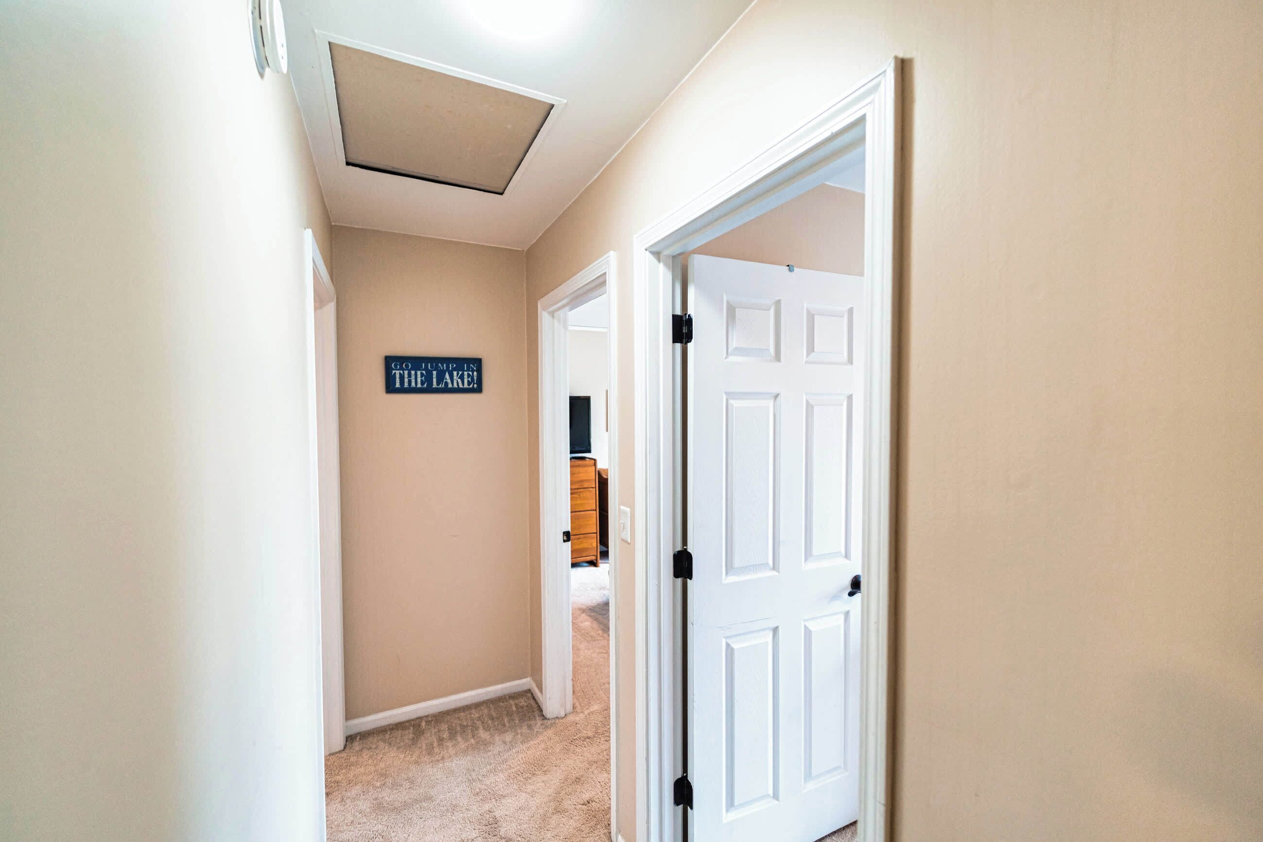 Un corridoio con pareti beige, una lampada a soffitto e una porta con il cartello che recita 'GO TO THE LAKE!'. 