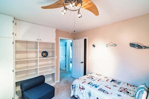 A bedroom with a bed, a wardrobe, a ceiling fan, and a door leading to another room.