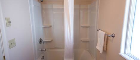 Ein Badezimmer mit Badewanne, Duschvorhang, Handtuchhalter und einem Fenster.