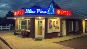 A motel named 'Blue Pine' with a neon sign, brick exterior, and a small porch area with a bench and flowers. - Blue Pine Motel (Panguitch)