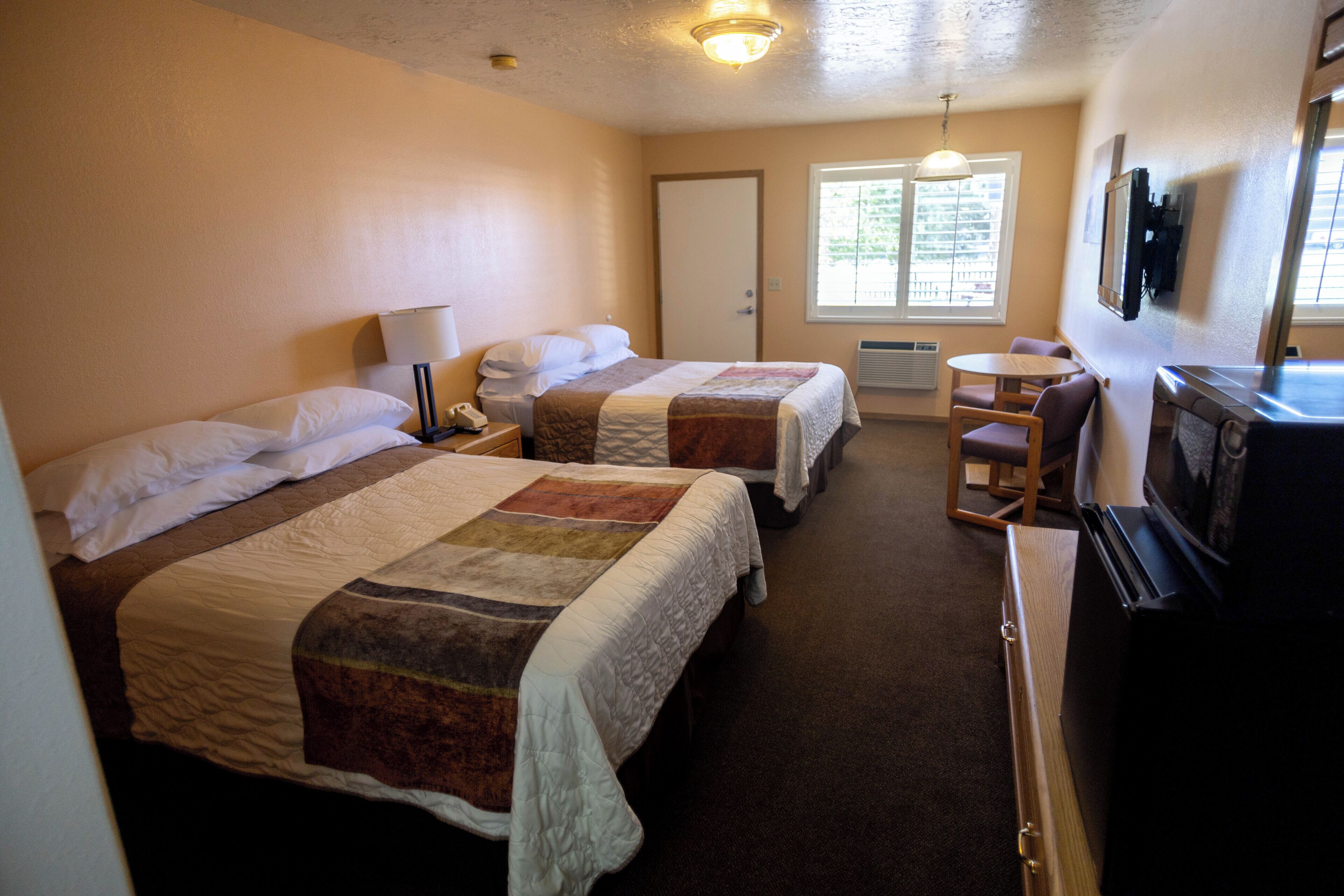 A hotel room with two beds, a desk, a chair, a television, and a window with blinds.