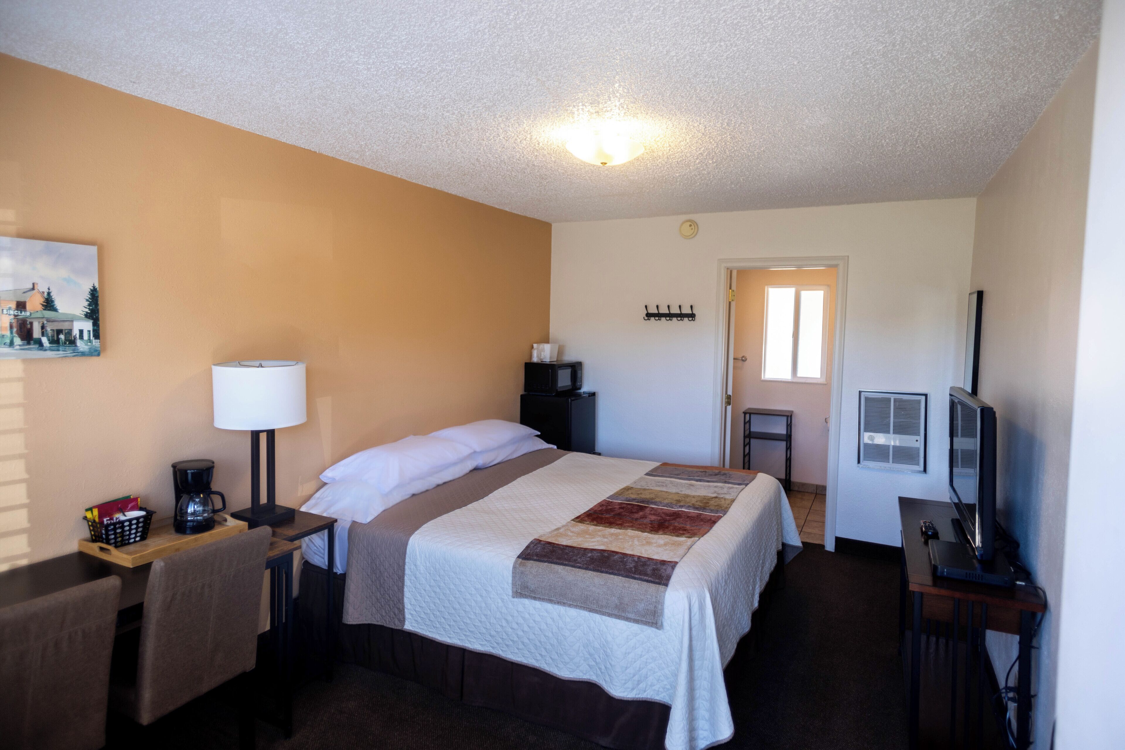 A hotel room with a bed, a desk with a lamp, a television, and a painting on the wall.