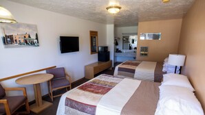 A hotel room with two beds, a small table, a chair, a television, and a painting on the wall. - Blue Pine Motel (Panguitch)