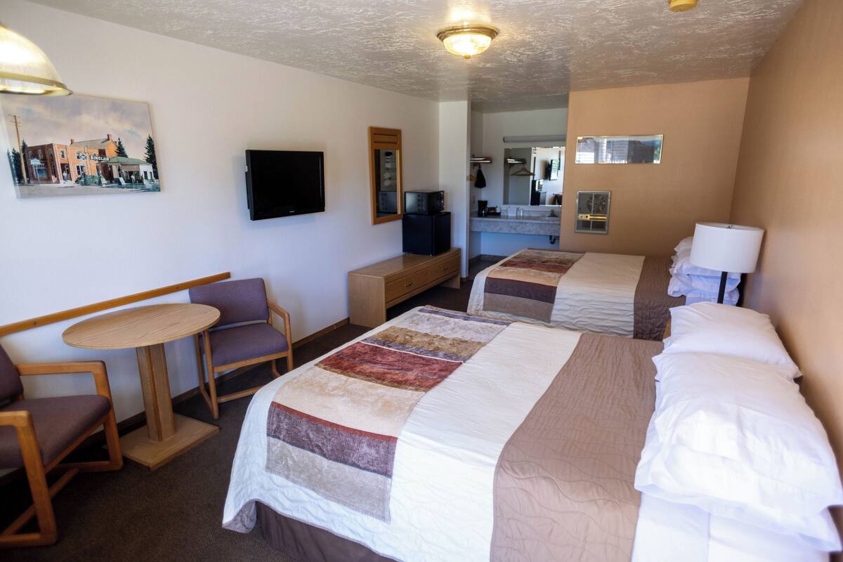 A hotel room with two beds, a small table, a chair, a television, and a painting on the wall.