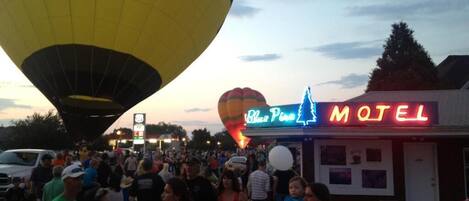 A motel with a neon sign, a hot air balloon in the background, and a crowd of people.