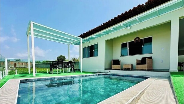 A swimming pool with a glass enclosure, a covered seating area, and a house with large windows.
