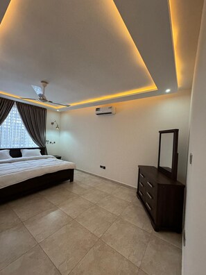 A modern bedroom with a bed, a dresser, a ceiling fan, and an air conditioning unit.