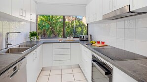 A modern kitchen with white cabinets, a stainless steel sink, and a window with a view of greenery. - 6 58 Pacific Drive Port Macquarie (Port Macquarie)