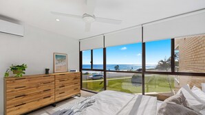 A bedroom with a large window, a bed, a wooden dresser, and a ceiling fan. - 6 58 Pacific Drive Port Macquarie (Port Macquarie)