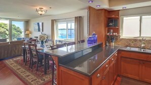 A modern kitchen with wooden cabinets, a large island, and a view of the sea.