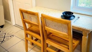A dining area with a white table and two wooden chairs with woven seats. A black bowl and spoon are on the table.