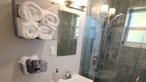 Un baño moderno con ducha envuelta en vidrio, inodoro, lavamanos y toallero con toallas dobladas cuidadosamente.