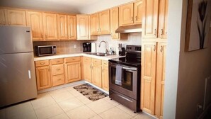 A kitchen with wooden cabinets, a stainless steel refrigerator, a microwave, a stove, and a sink.