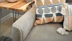 A modern living room with a grey sofa, a wooden side table, a white lamp, and decorative pillows.