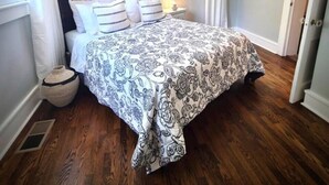 A bedroom with a bed, a window with curtains, a painting on the wall, and a wooden floor.