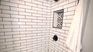 A bathroom with white subway tiles, a white bathtub, a towel hanging on the wall, and a black showerhead.