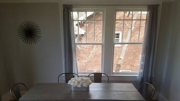 A dining room with a wooden table, four chairs, a vase of flowers, and a window with curtains. - 10 Historic Earle with Rustic Charm (Greenville)