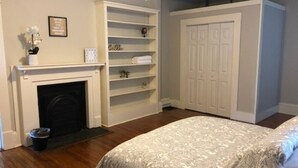 Quarto com lareira, prateleiras embutidas, guarda-roupa e cama com colcha estampada.
