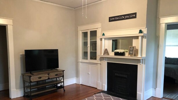 Uma sala de estar com lareira, uma televisão sobre um suporte de madeira, e um letreiro acima da lareira com a frase 'love the life you live'.