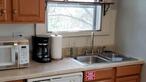 Una cocina funcional con armarios de madera, microondas integrado, cafetera, lavavajillas y una ventana sobre el fregadero.