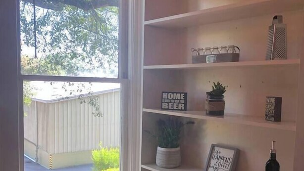 Una habitación con un ventanal grande, una pared blanca y una estantería empotrada con varios objetos.
