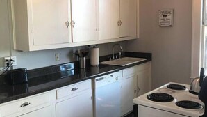 Una cocina con armarios blancos, encimera negra, estufa y lámpara colgante.