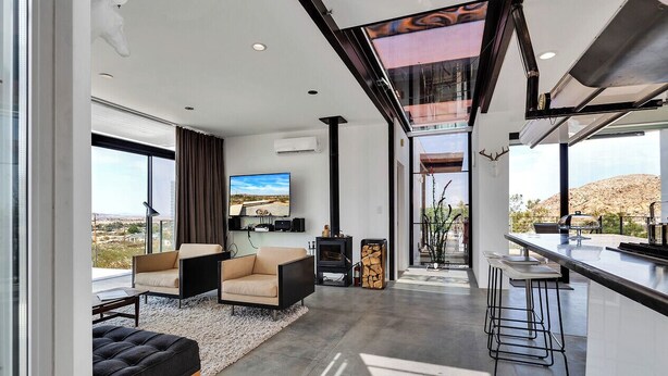 Uma sala de estar moderna com uma televisão grande, assentos confortáveis, lareira e vista para a paisagem desértica.