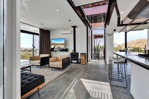 A modern living room with a large TV, comfortable seating, a fireplace, and a view of the desert landscape. - School House 2 Bedroom 2 Bath  (Joshua Tree)