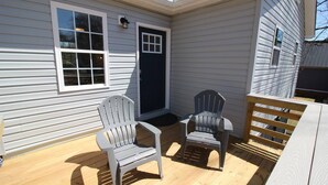 Eine Terrasse mit zwei Adirondack-Stühlen, einem Holzzaun und einem Haus mit weißem Farbton und einer dunkel gefärbten Haustür.